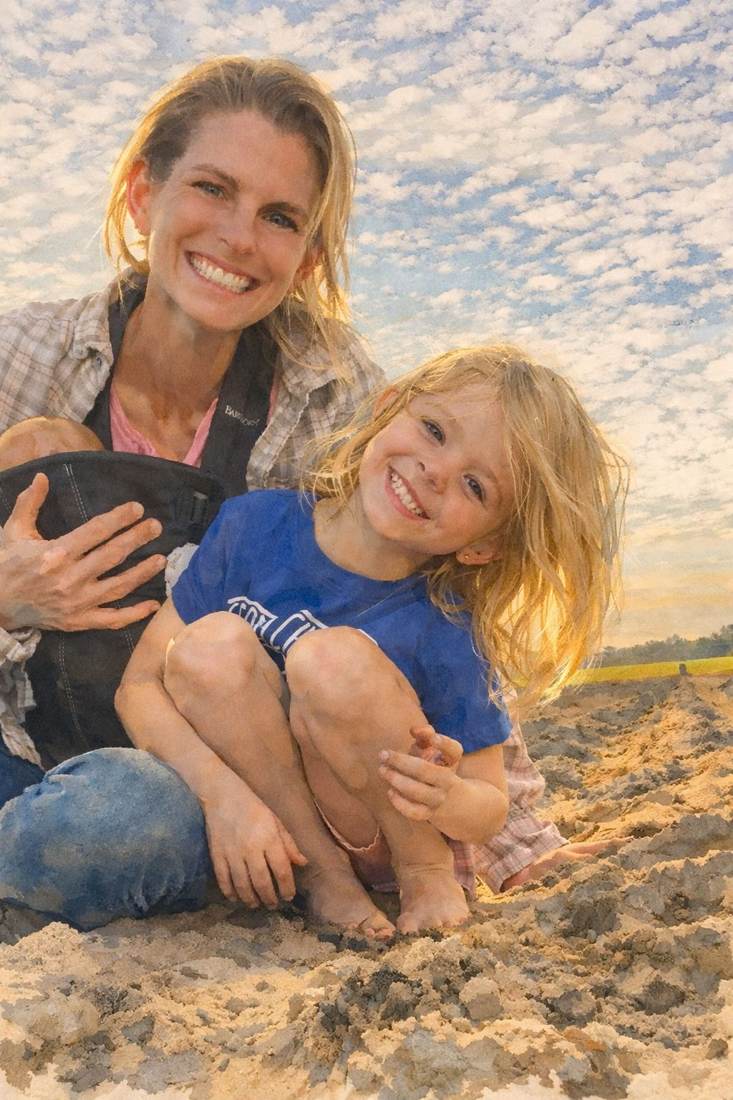 A mother and daughter smiling together in the field at golden hour